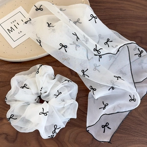 Détail de chouchou en mousseline blanche et ruban avec motif nœud noir sur bois