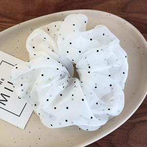 Détail d'un chouchou en tulle blanc à pois sur un plateau en céramique et bois