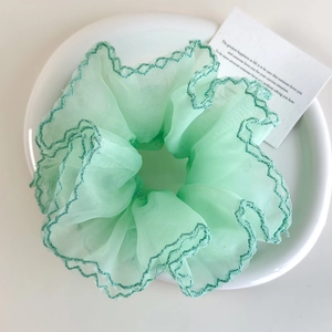 Détail du chouchou en organza vert clair avec bords à volants vert foncé sur assiette
