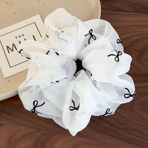 Détail d'un chouchou en organza blanc avec motif de nœud noir sur plateau en céramique