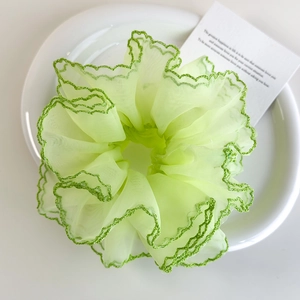 Détail d'un grand chouchou en organza vert clair avec des bords à volants vert foncé