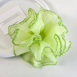 Détail d'un chouchou en organza vert clair avec coutures fines sur une assiette blanche