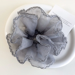 Détail macro du chouchou en organza gris avec bords volantés argentés sur une assiette