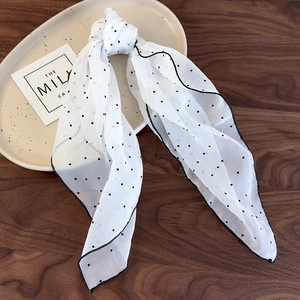 Détail d'un foulard en tulle blanc à pois noirs posé sur un fond en bois