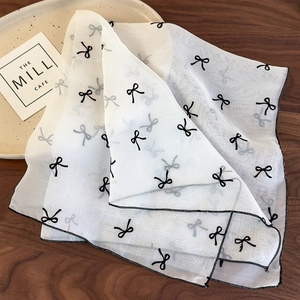 Détail d'un foulard en résille blanche avec motifs nœuds noirs et couture sur table en bois
