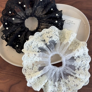 Détail d'un chouchou en dentelle blanche avec broderie florale et perles sur céramique