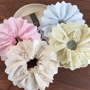Detailed view of four pastel embroidered lace scrunchies in a white ceramic dish