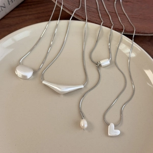 Matte silver snake chain necklaces with heart and geometric pendants on a ceramic plate