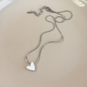 Close-up of silver snake chain with heart pendant on minimalist ceramic tray