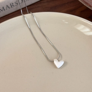 Detail of matte silver heart pendant on a snake chain over a minimalist ceramic plate