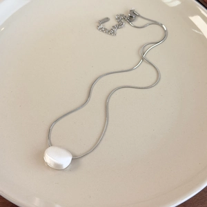 Macro detail of silver snake chain with oval brushed metal pendant on ceramic plate