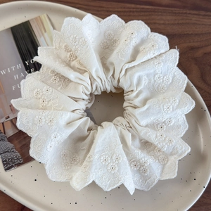 Close-up of ivory floral embroidery and scalloped lace edges on a hair scrunchie