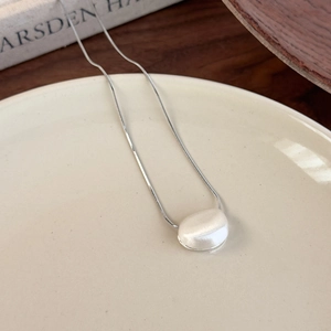 Detailed close-up of a silver brushed pebble pendant on a snake chain over ceramic