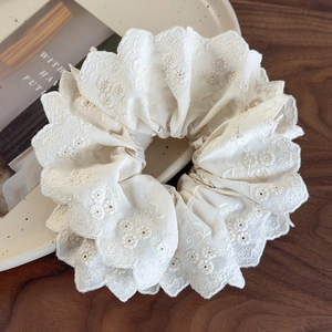Detail of off-white lace hair scrunchie with intricate floral embroidery and scalloped edges