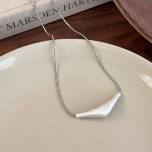 Minimalist silver snake chain necklace with curved tubular pendant on ceramic plate