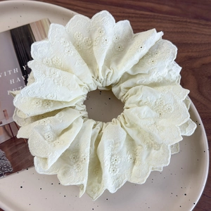 Detailed close-up of cream floral embroidery and hollow scallop edges on a lace scrunchie