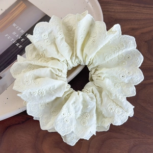 Close-up of cream embroidered floral lace scrunchie with scalloped edges on ceramic tray