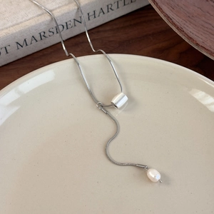 Close-up of silver snake chain necklace with pearl pendant on a ceramic dish