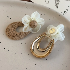Detail of handmade woven straw earrings with mesh flowers and golden alloy base