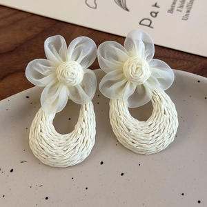 Close-up of handmade woven flower earrings with cream mesh petals on a matte tray