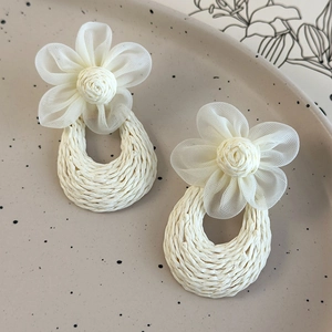 Macro view of handmade cream floral drop earrings with woven raffia teardrop pendants
