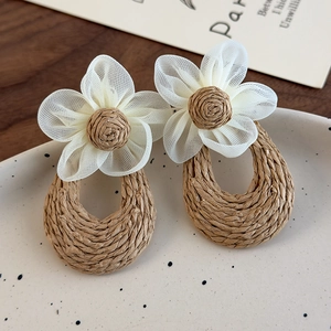 Detail of handmade straw woven earrings with mesh flowers and teardrop pendants