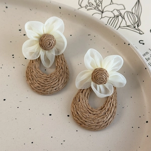 Detailed shot of handmade woven flower earrings on a beige ceramic tray accessory