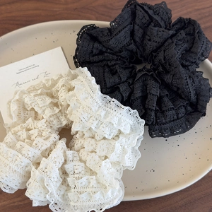 Close-up of layered lace scrunchies in black and beige on a ceramic plate