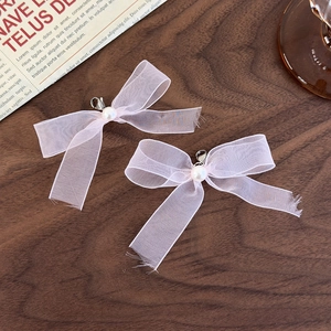 Close-up of pink sheer ribbon bows with white pearl and metal clasp on wood background