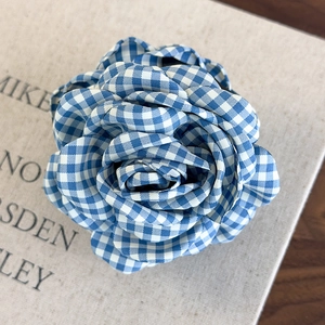 Detail of a blue and white gingham fabric rose hair clip with layered 3D petal textures