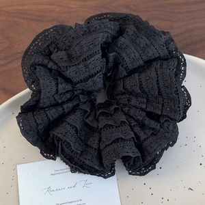 Detail of black layered lace scrunchie with pleated texture on a ceramic plate