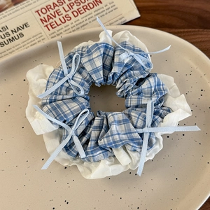 Detail of blue plaid hair scrunchie with lace trim and bows on a ceramic plate