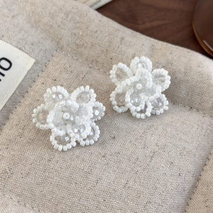 Detailed close-up of handmade white beaded flower earrings on a beige fabric pouch