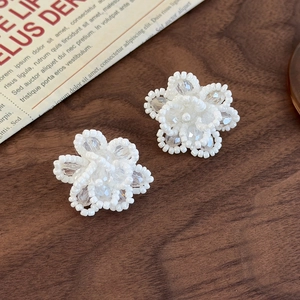 Macro shot of handmade white beaded flower earrings on a vintage walnut wood surface