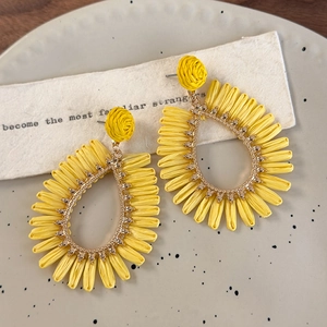 Detailed view of yellow raffia teardrop earrings with gold metal trim for vacation