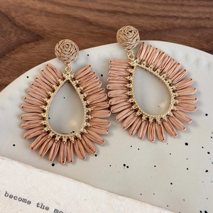 Detail of bohemian hollow teardrop woven straw earrings with gold alloy beads