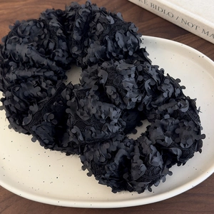 Détail d'un chouchou floral noir avec pétales en mesh 3D sur une assiette décorative
