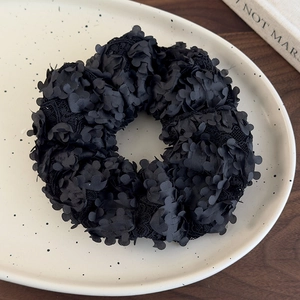 Gros plan détaillé d'un chouchou en maille noire avec pétales de fleurs 3D sur assiette