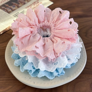 Three embroidered lace scrunchies in pink, white, and blue colors on a ceramic plate