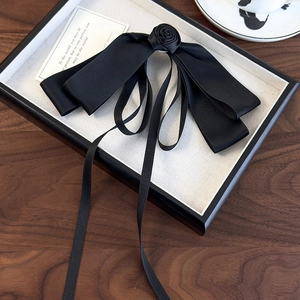 Detail view of a vintage black satin bow hair clip with a handmade rose on a display tray