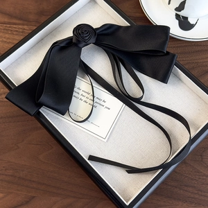 Detail of black satin bow hair clip with rose decoration and long ribbons on tray