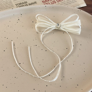 Close-up of ivory ribbon bow hair clip with sparkling rhinestone and long tassels