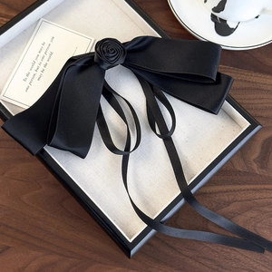 Detailed view of a black satin bow hair clip with a handmade rose and flowing ribbons