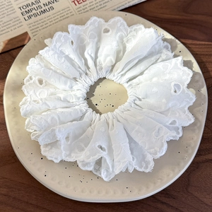 Detail of white embroidered lace scrunchie with hollow heart patterns on a ceramic plate