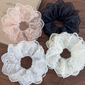 Close-up of four floral lace scrunchies in pink, black, and white on a wooden surface