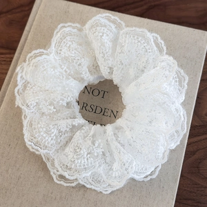 Close-up of white lace scrunchie with floral embroidery and delicate mesh texture