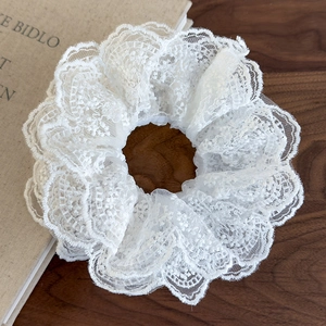 Close-up of white layered lace scrunchie showing fine floral embroidery on wood