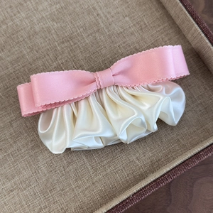 Detail der rosa Schleifen-Haarspange mit cremeweißer Satinbasis auf Flechttablett