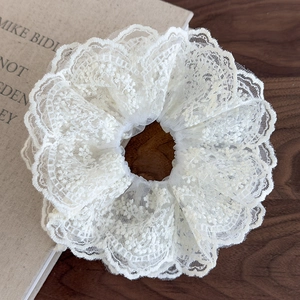 Macro view of multi-layered cream lace hair scrunchie with intricate embroidery details