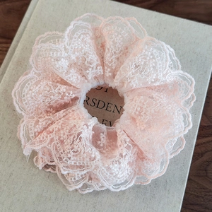 Close-up of layered pale pink lace scrunchie with intricate embroidery on a book
